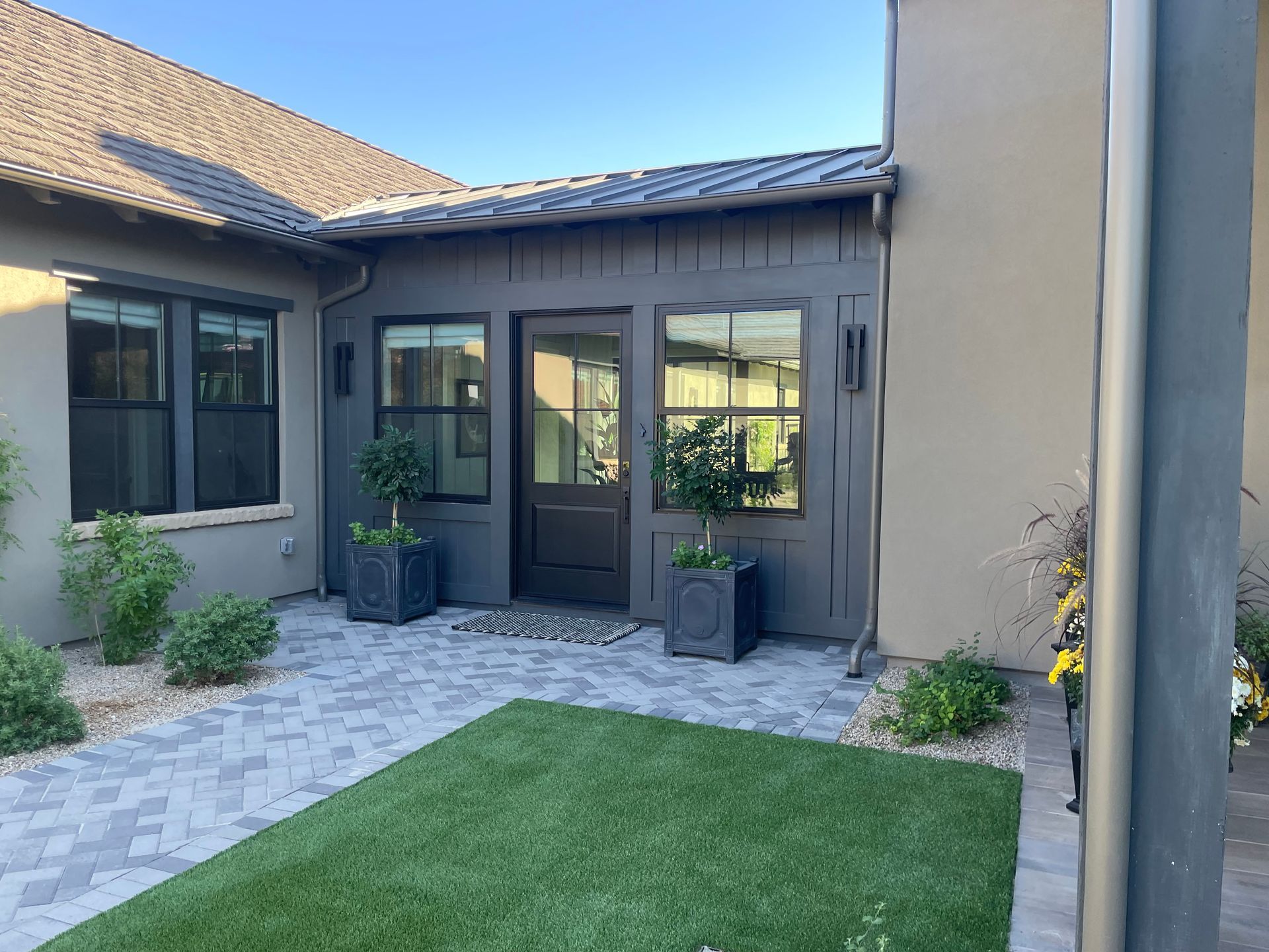 Courtyard patio with gray pavers, artificial grass, black-framed doors, and potted plants