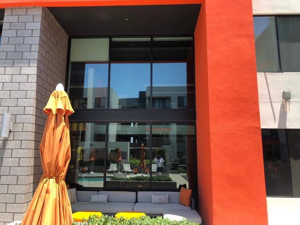 Modern building entrance with large glass doors, orange facade, and closed patio umbrella in front