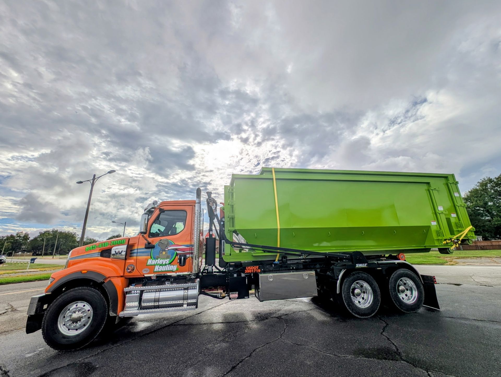 Orange dump truck with a bright green bed parked on a road under a cloudy sky