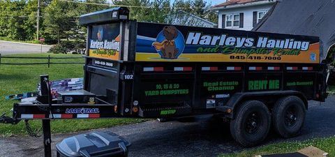 Harleys Hauling dump trailer parked on grass, black with orange lettering and logo