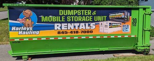 Green dumpster with a mobile storage unit rentals advertisement and phone number on the side.