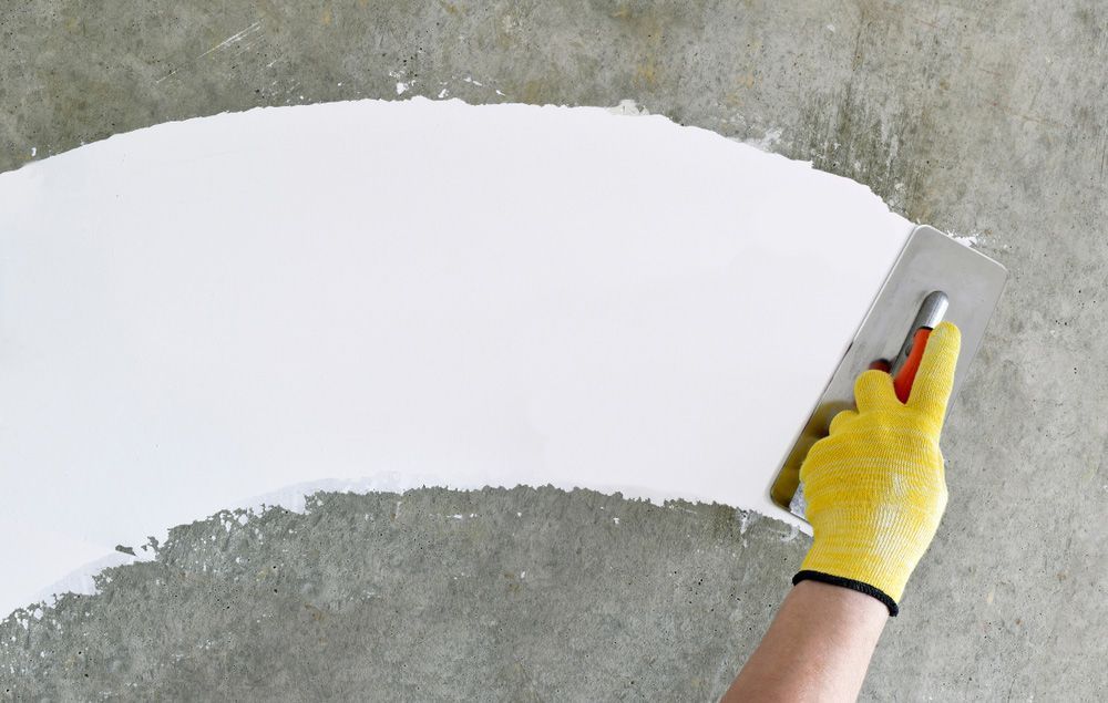A Person Is Using A Spatula To Spread White Paint On A Concrete Surface — Mid Coast Coatings In Kempsey, NSW