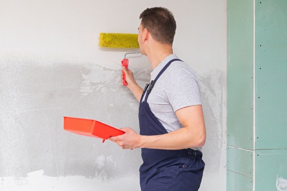 A Man Is Painting A Wall With A Paint Roller — Mid Coast Coatings In Kempsey, NSW