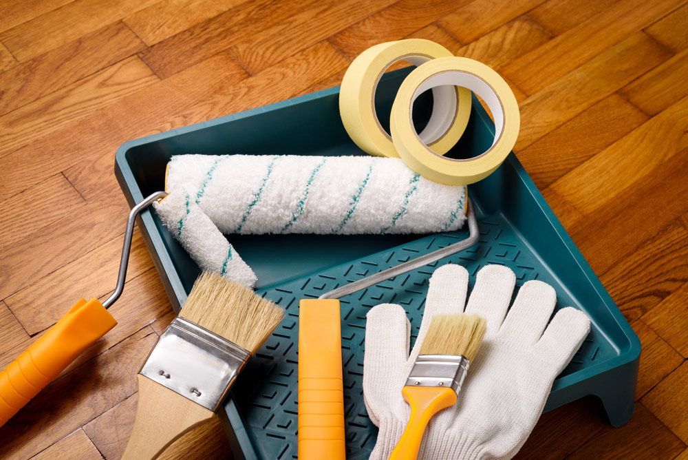 A Tray With Paint Rollers Brushes Tape And Gloves On A Wooden Floor — Mid Coast Coatings In Kempsey, NSW