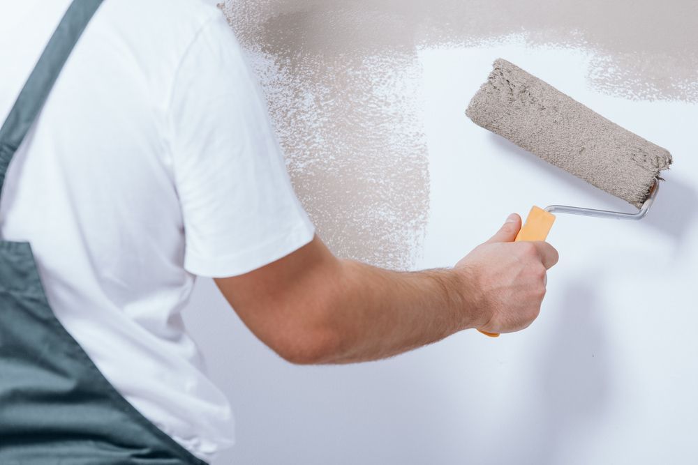 A Man Is Painting A Wall With A Paint Roller — Mid Coast Coatings In South West Rocks, NSW