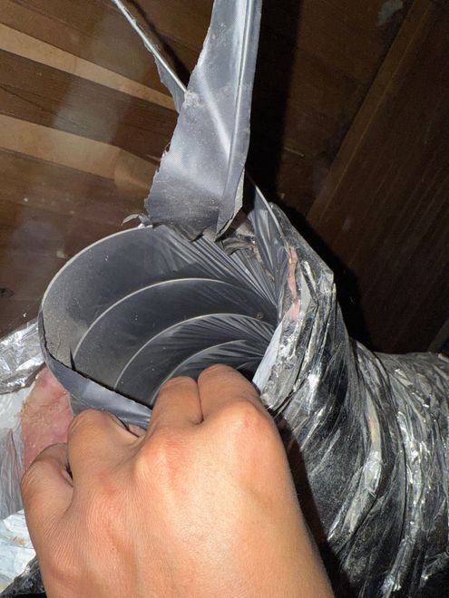 Hand holding a black duct-taped plastic tube or hose with a white ribbon tied around it