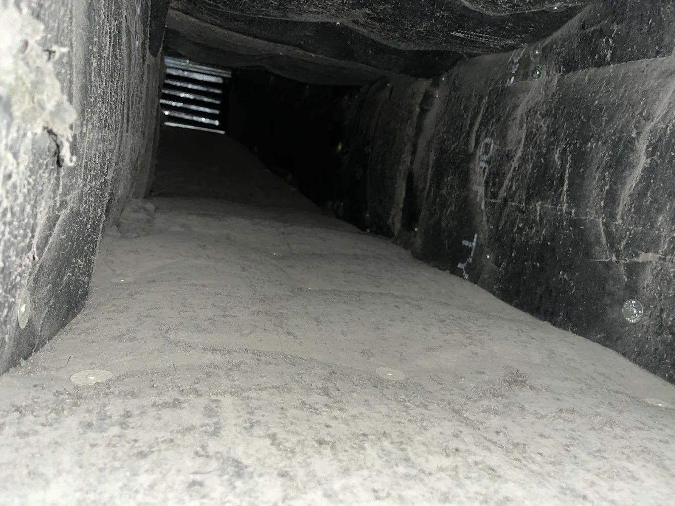 Narrow rocky tunnel with a sloped sandy floor and light at the far end