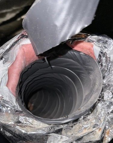 A black flexible pipe opening wrapped in foil tape, held above a dark circular duct.