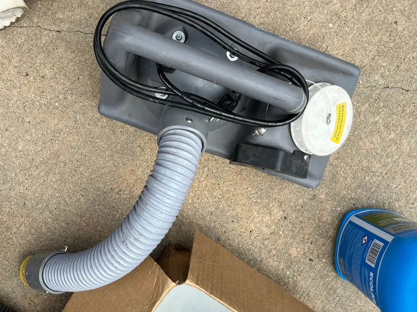 Portable gray dust collector with hose on a concrete floor, beside a blue bucket and cardboard box