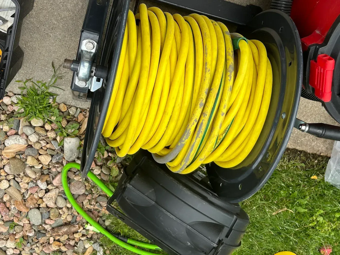 Yellow hose coiled on a black hose reel sitting on grass and gravel outdoors