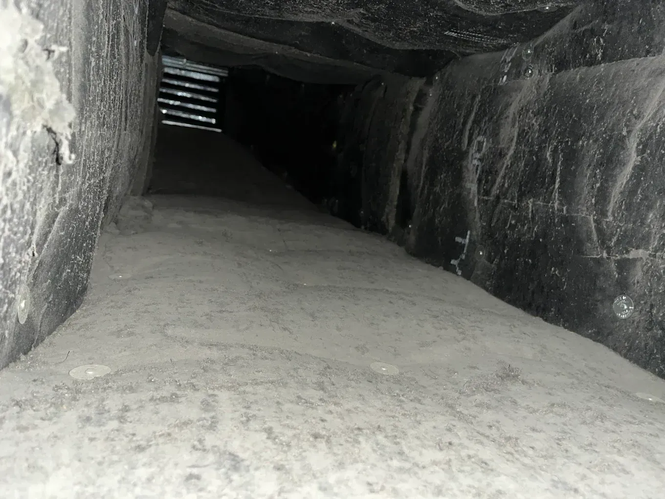 Dim rocky tunnel with a sandy floor and light entering from an opening at the far end