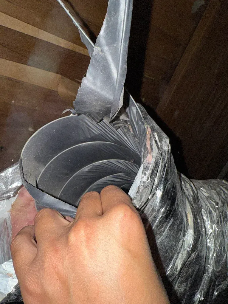 Hand holding a rolled gray duct-taped tube attached to a strap in a wooden-walled space