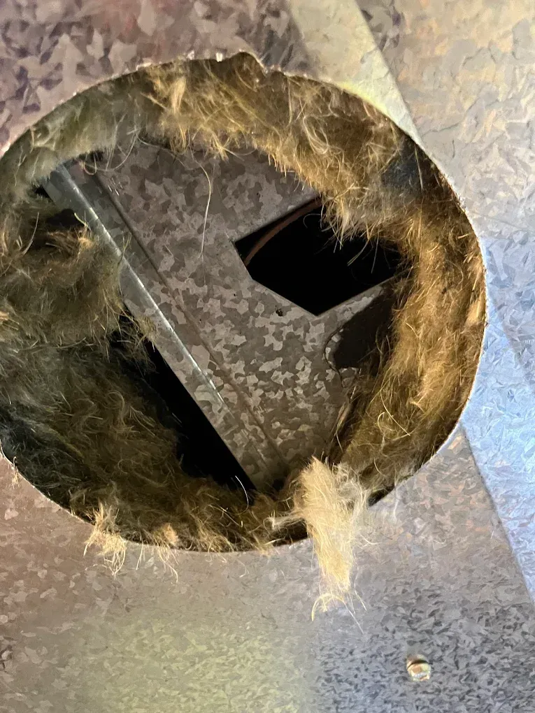 Circular metal opening with a black square vent inside, surrounded by scratched silver surface.