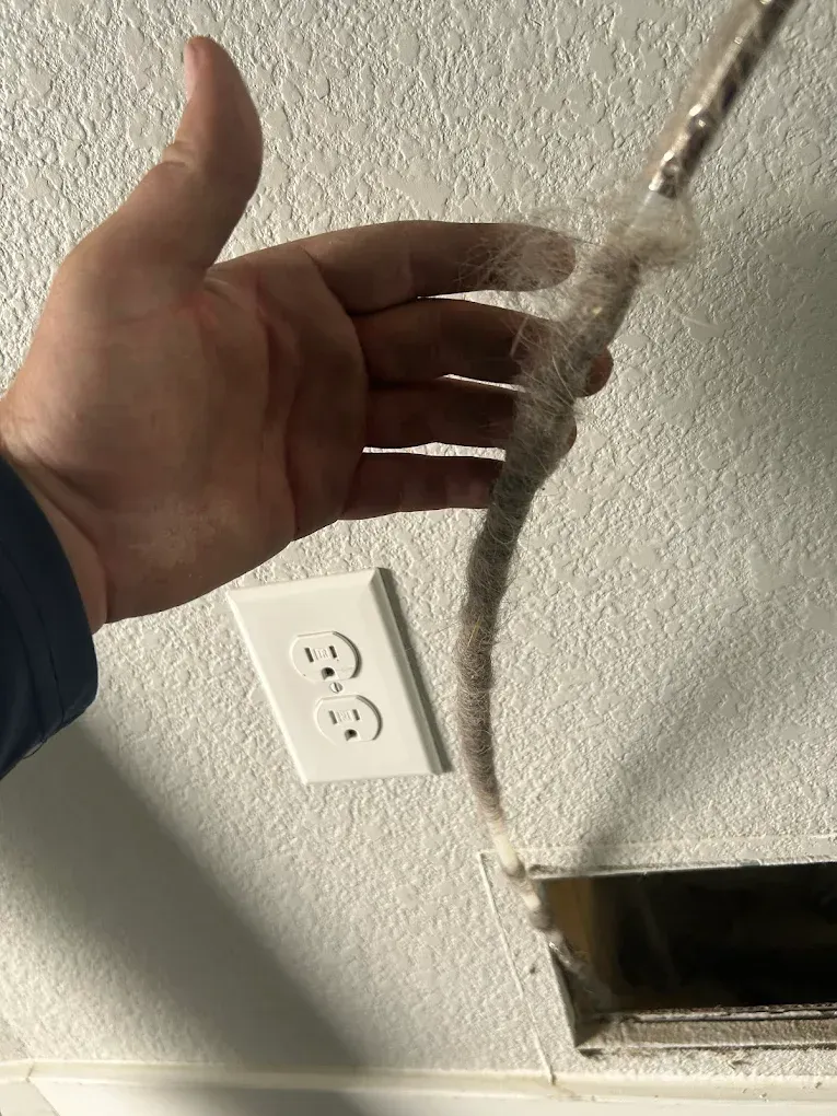 Hand reaching toward a hanging frayed cable beside a wall outlet and ceiling hole