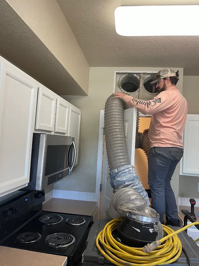 Man installing a large silver ventilation hose in a kitchen ceiling vent above a stove.