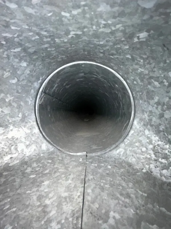 Looking down into a dark metal pipe with a gray, textured interior