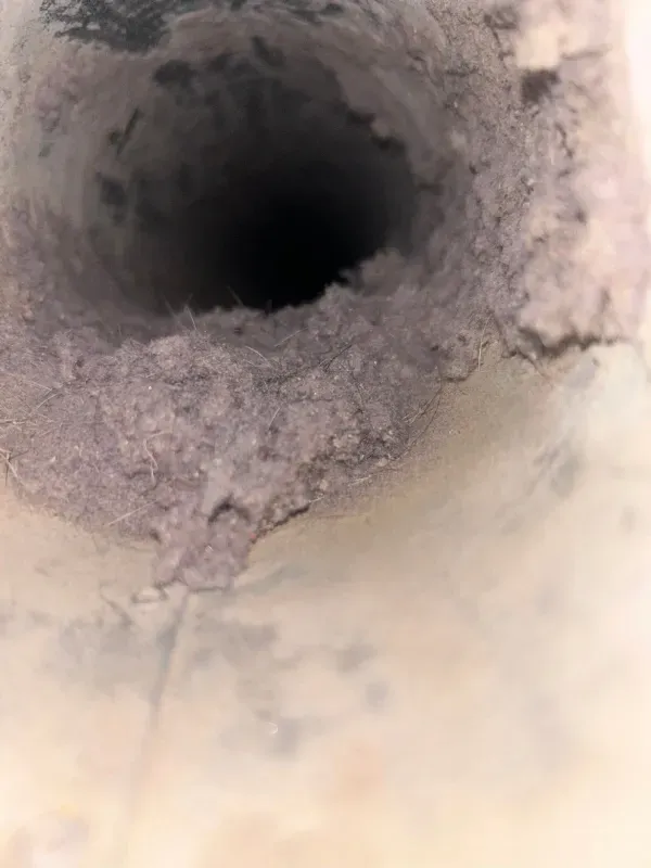 Close-up of a dark, dusty hole in a gray surface with rough debris around the opening