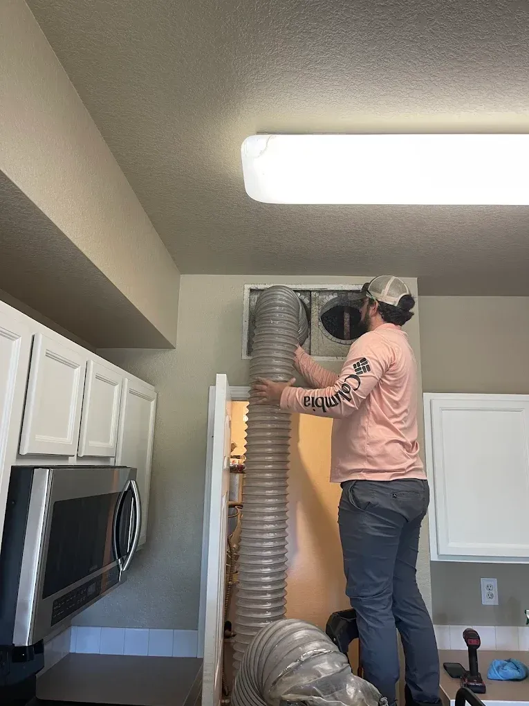 Person standing on a stool installing a silver vent hose in a kitchen ceiling opening