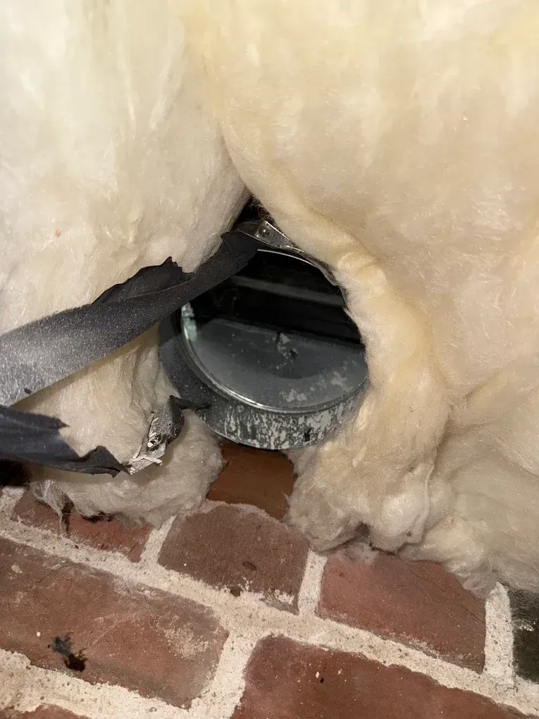 Broken vent duct surrounded by yellow insulation above a brick floor