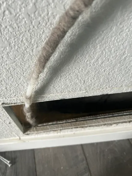 Close-up of a textured wall with a frayed cable or rope hanging from a vent opening