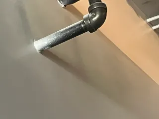 Black metal pipe elbow attached to a wall, with a short horizontal pipe extending out.