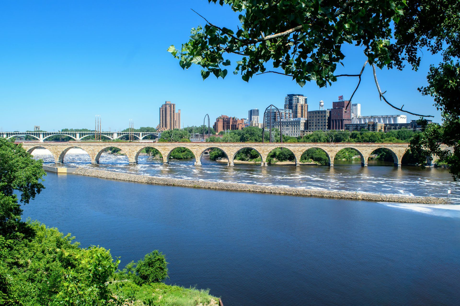 Stone bridge over a river with city skyline under a clear blue sky