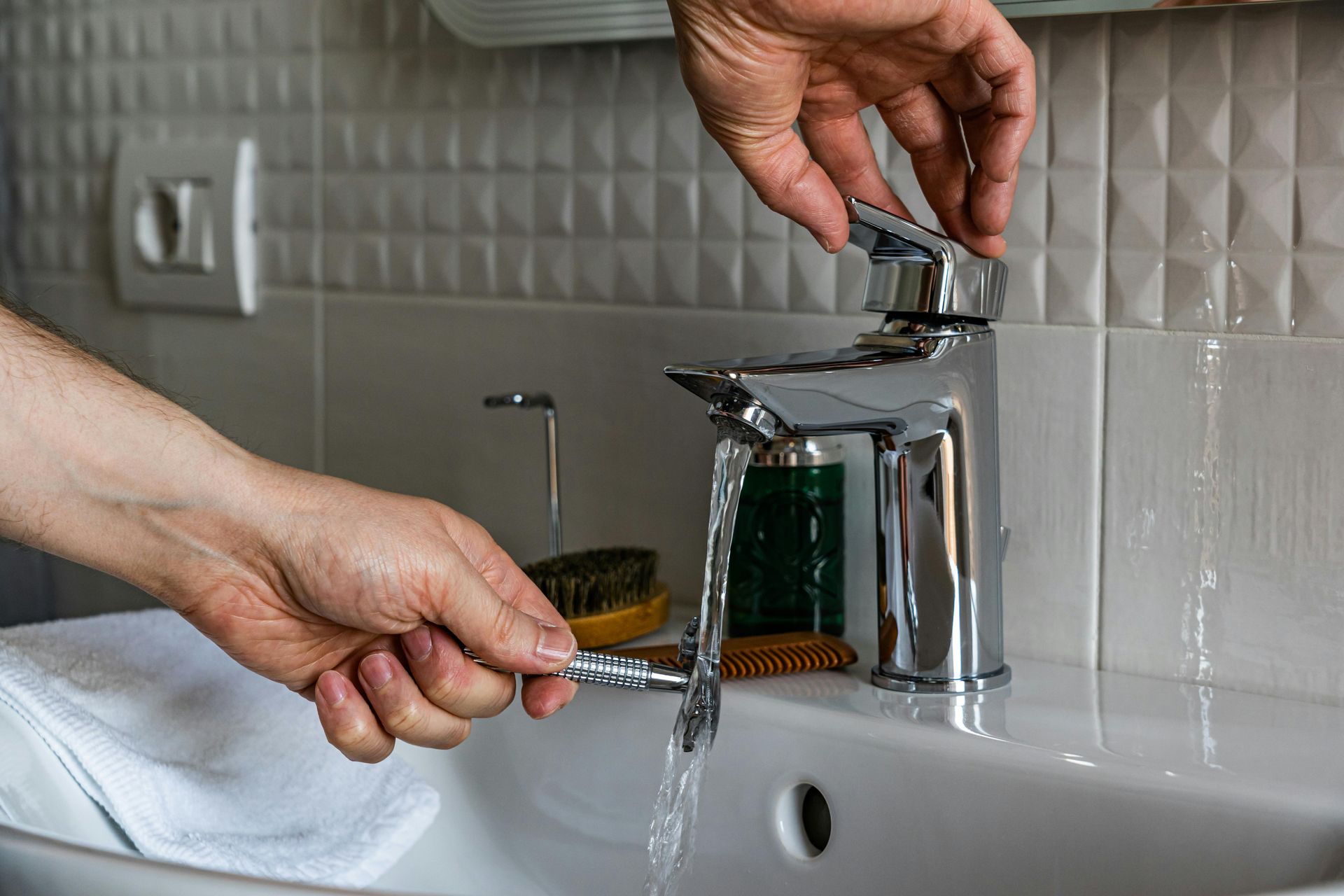 Hands turning on a chrome bathroom faucet as water runs into a white sink