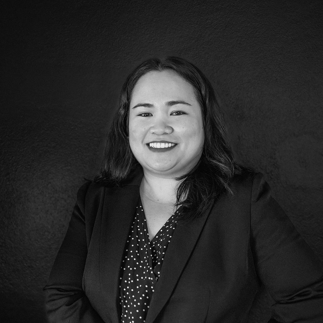 Smiling woman with dark hair, wearing a blazer and polka-dot shirt, poses against a dark background.