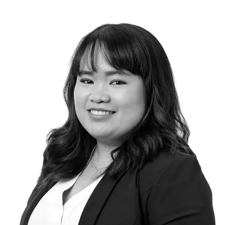 Smiling Asian woman in a blazer, white shirt, and dark hair; studio portrait.