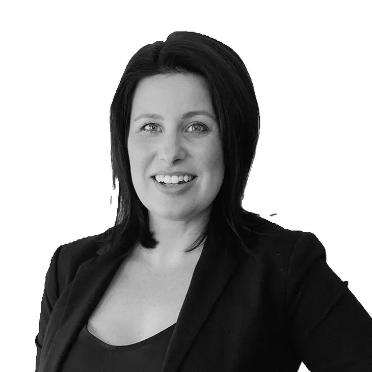 Woman with dark hair and a blazer, smiling, in a studio setting.