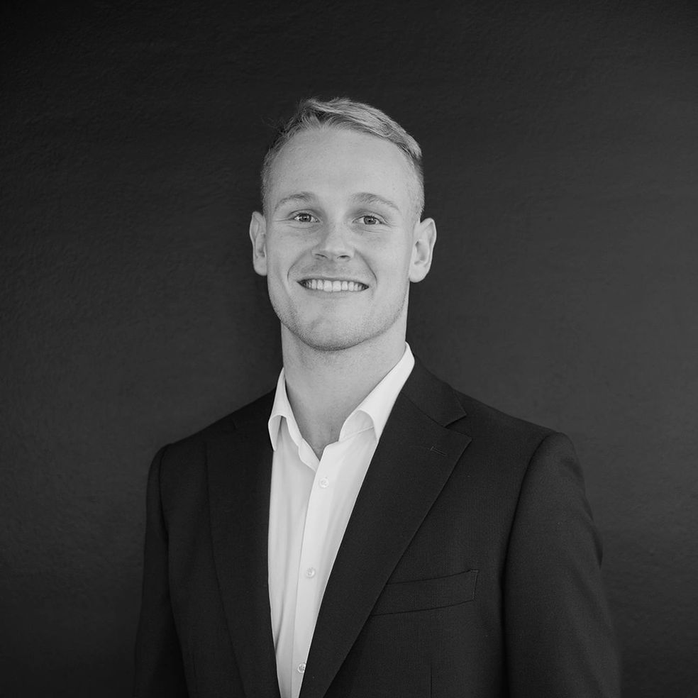 Young man in a suit smiling at the camera against a dark background.
