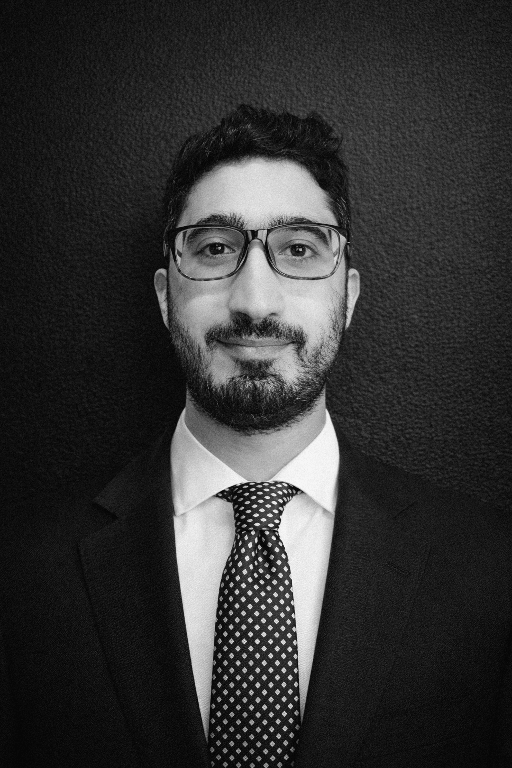 Man with glasses and beard in a suit, looking at the camera.