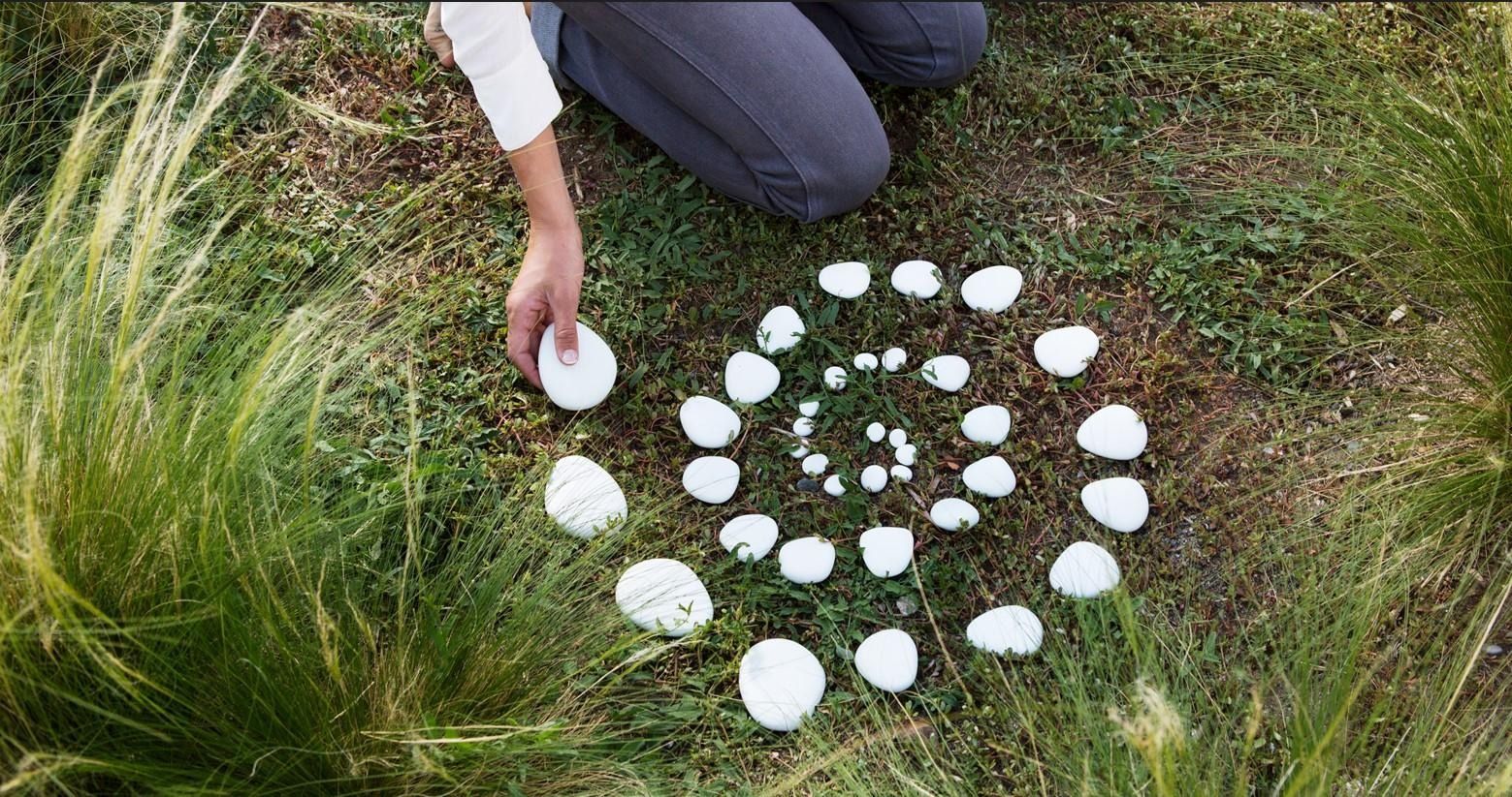 Person arranging white stones in a spiral pattern on grass outdoors