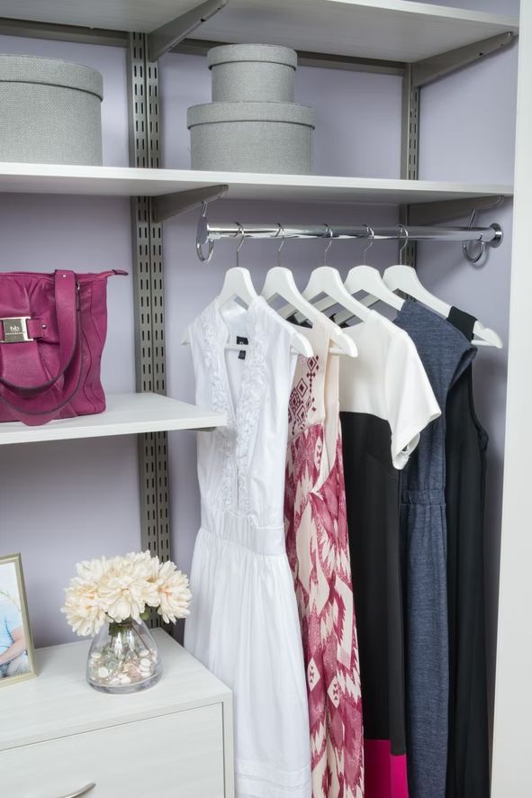 Closet shelf with hanging dresses, white storage boxes, pink bag, and a small dresser with flowers.
