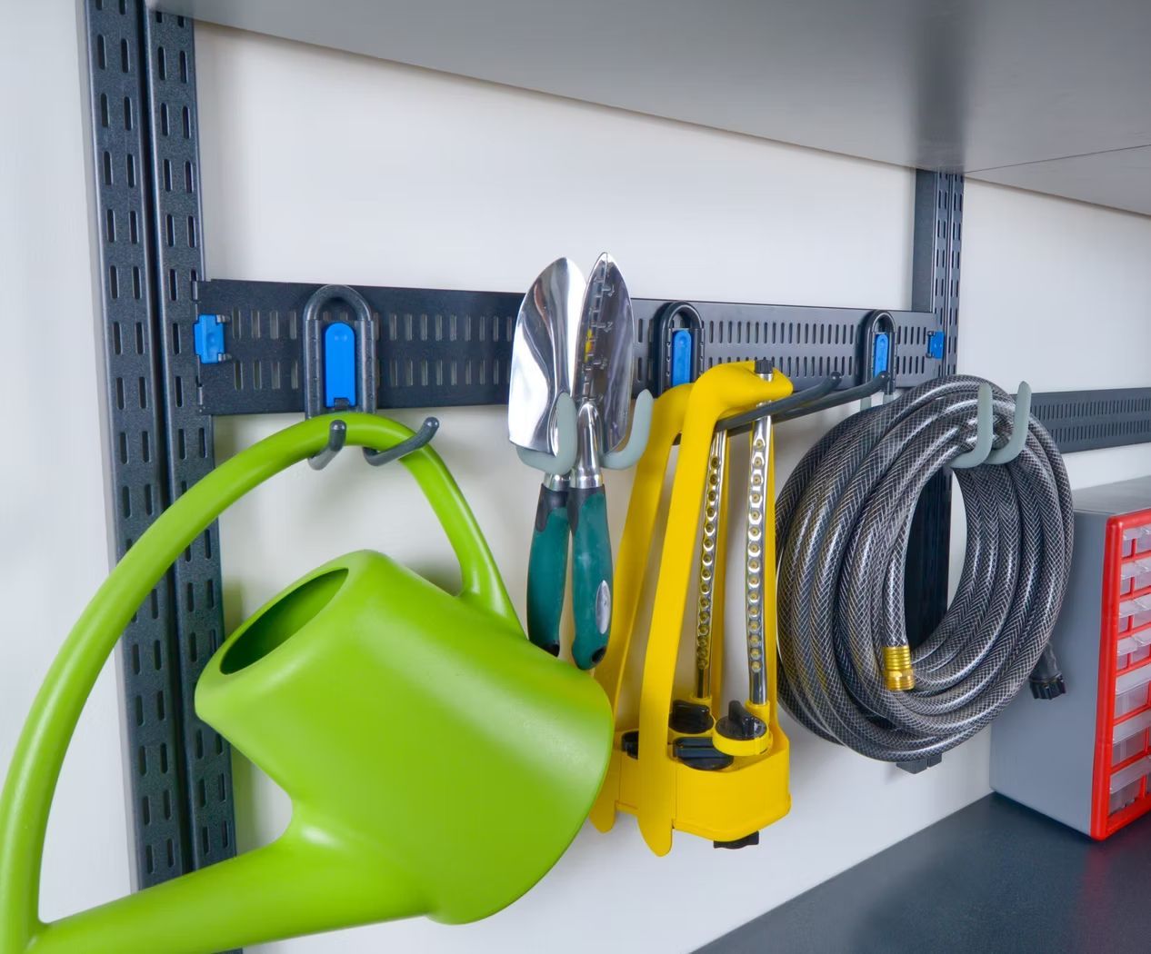 Green watering can, yellow tools, and coiled rope on a gray workshop shelf