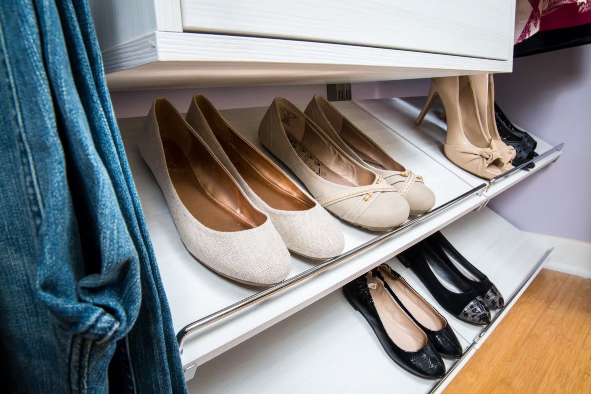 Shoes neatly arranged on white closet shelves, with blue hanging clothes at left.