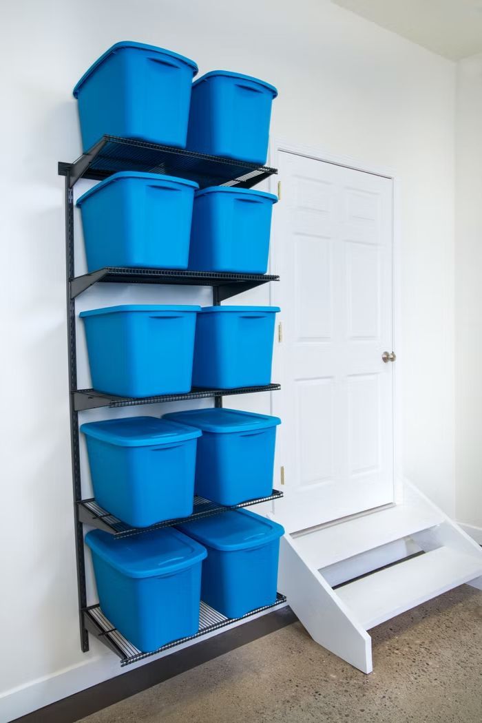 Blue storage bins on wall shelves beside a white door and small step stool in a carpeted room