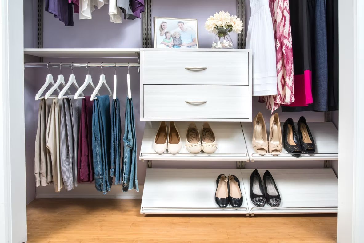Open closet with white drawers, hanging clothes, shoes, and folded items on shelves