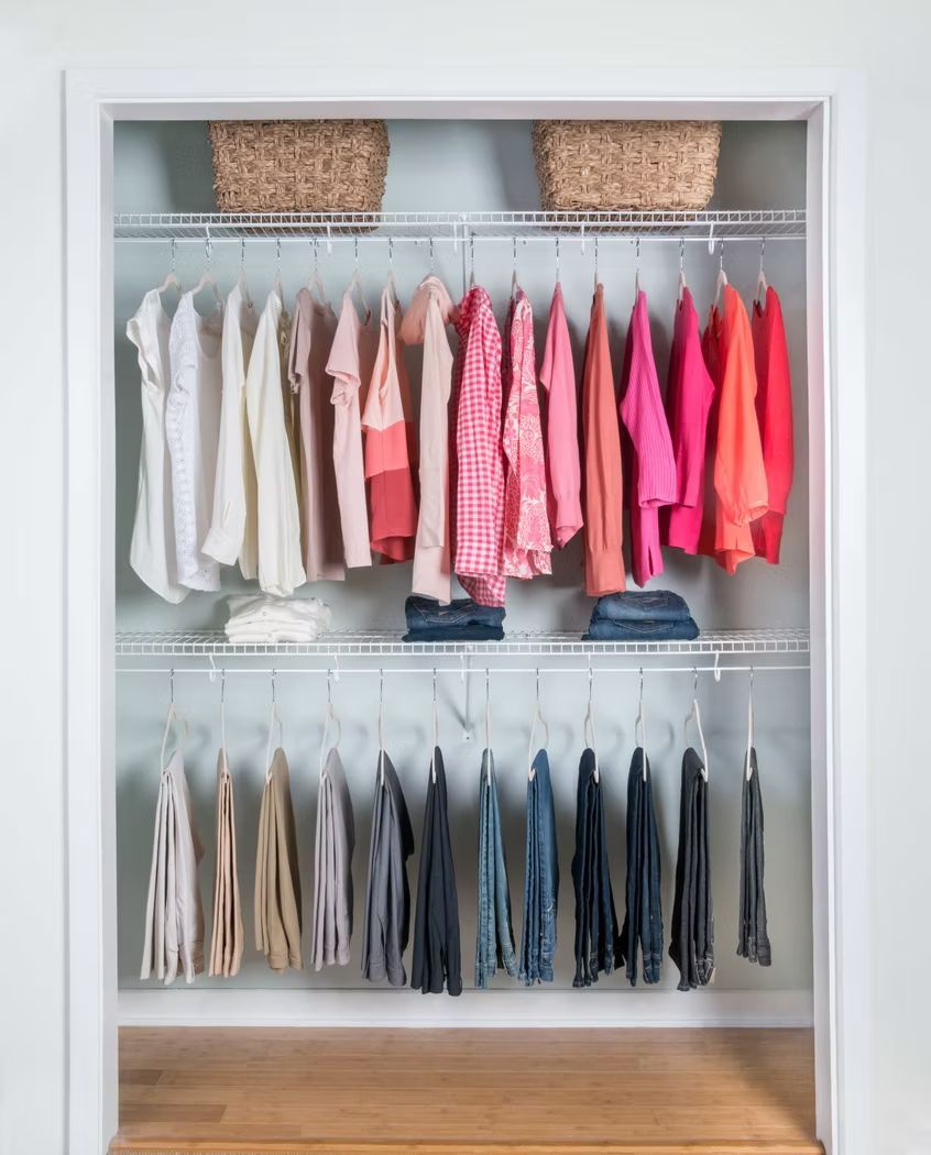 Built-in closet with neatly hung white, pink, and gray clothes and two woven storage baskets on top shelves