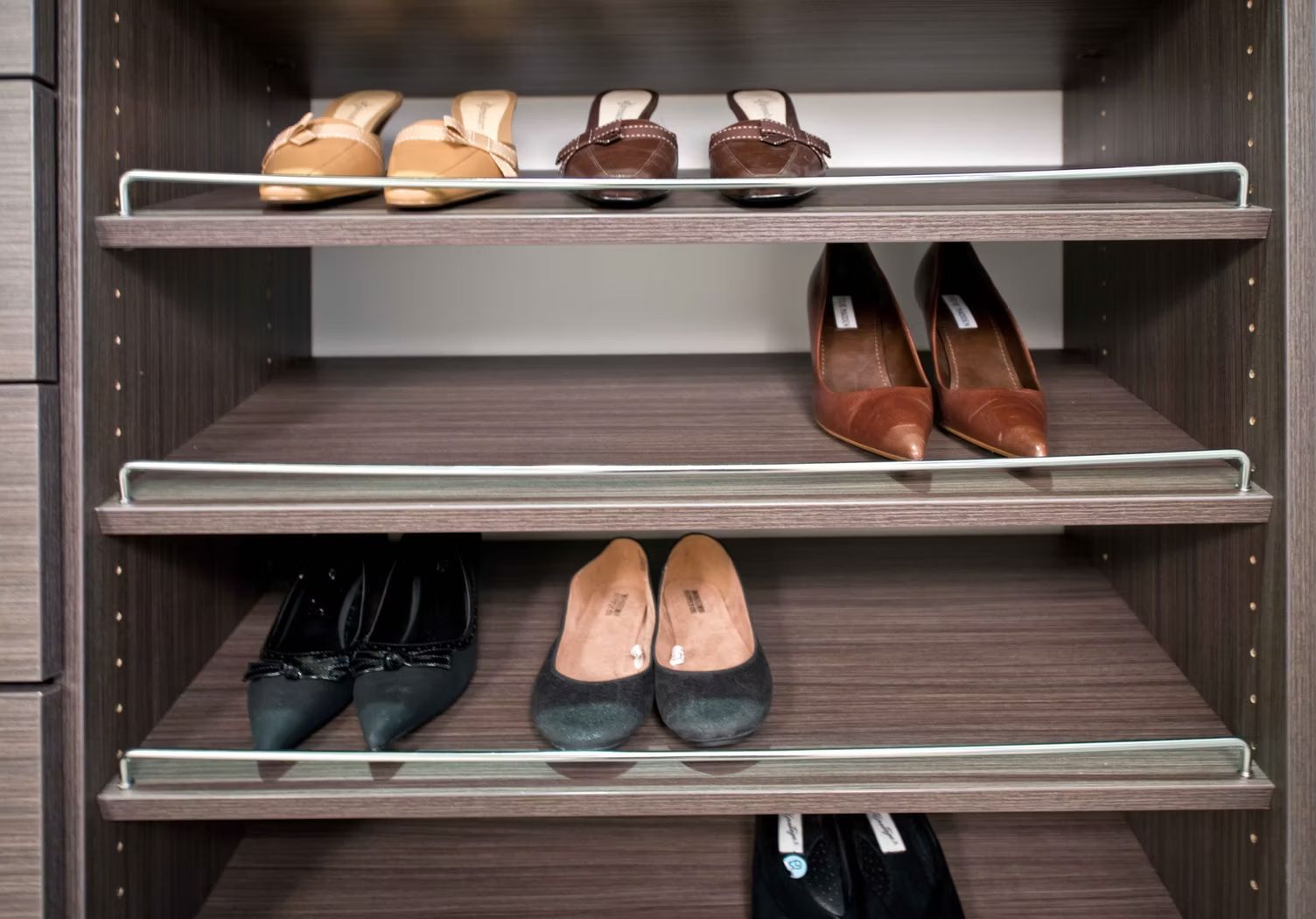 Shoe rack with several pairs of dress shoes on three shelves in a closet