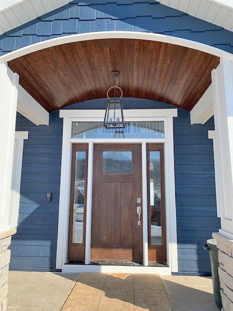 Front entry with dark wood door, blue siding, white trim, and a curved wood porch ceiling