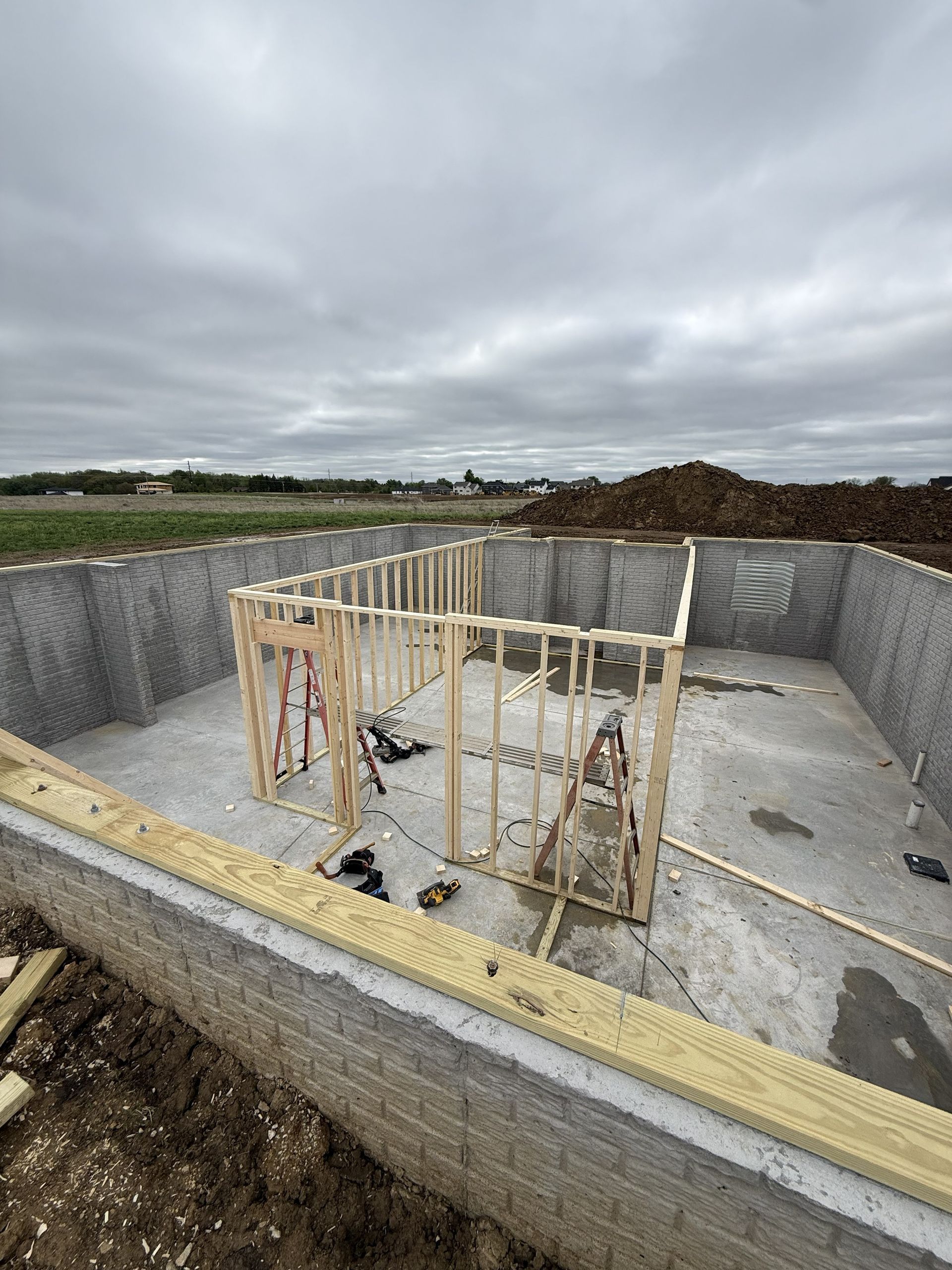 Concrete construction pit with rebar cage and trench, under overcast sky