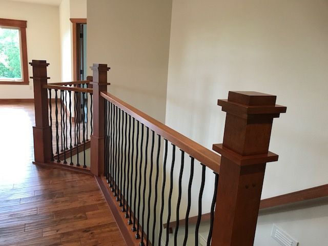 Wooden staircase landing with black wrought-iron railing and hardwood floor in a bright hallway