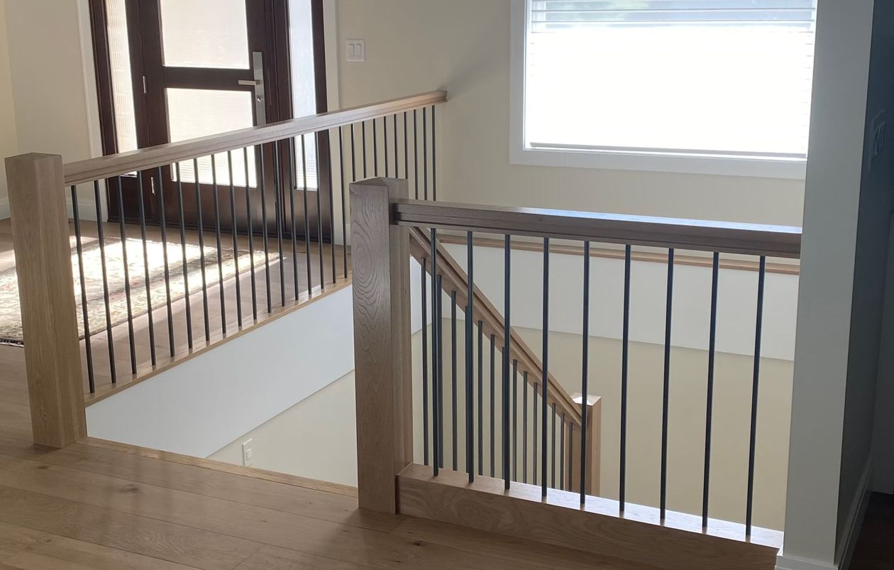 Staircase landing with wooden railings and white walls, lit by a window on the right.