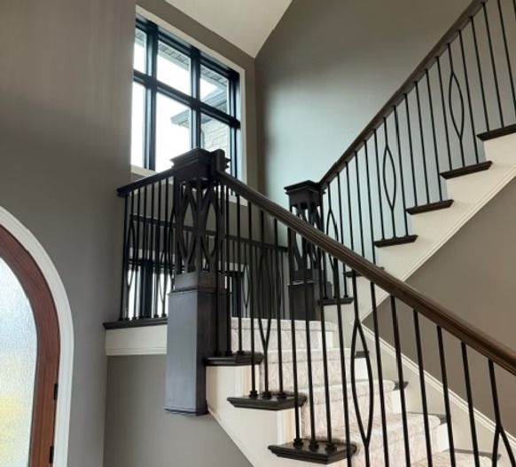 Interior staircase with black railings, white walls, and a large arched window below.