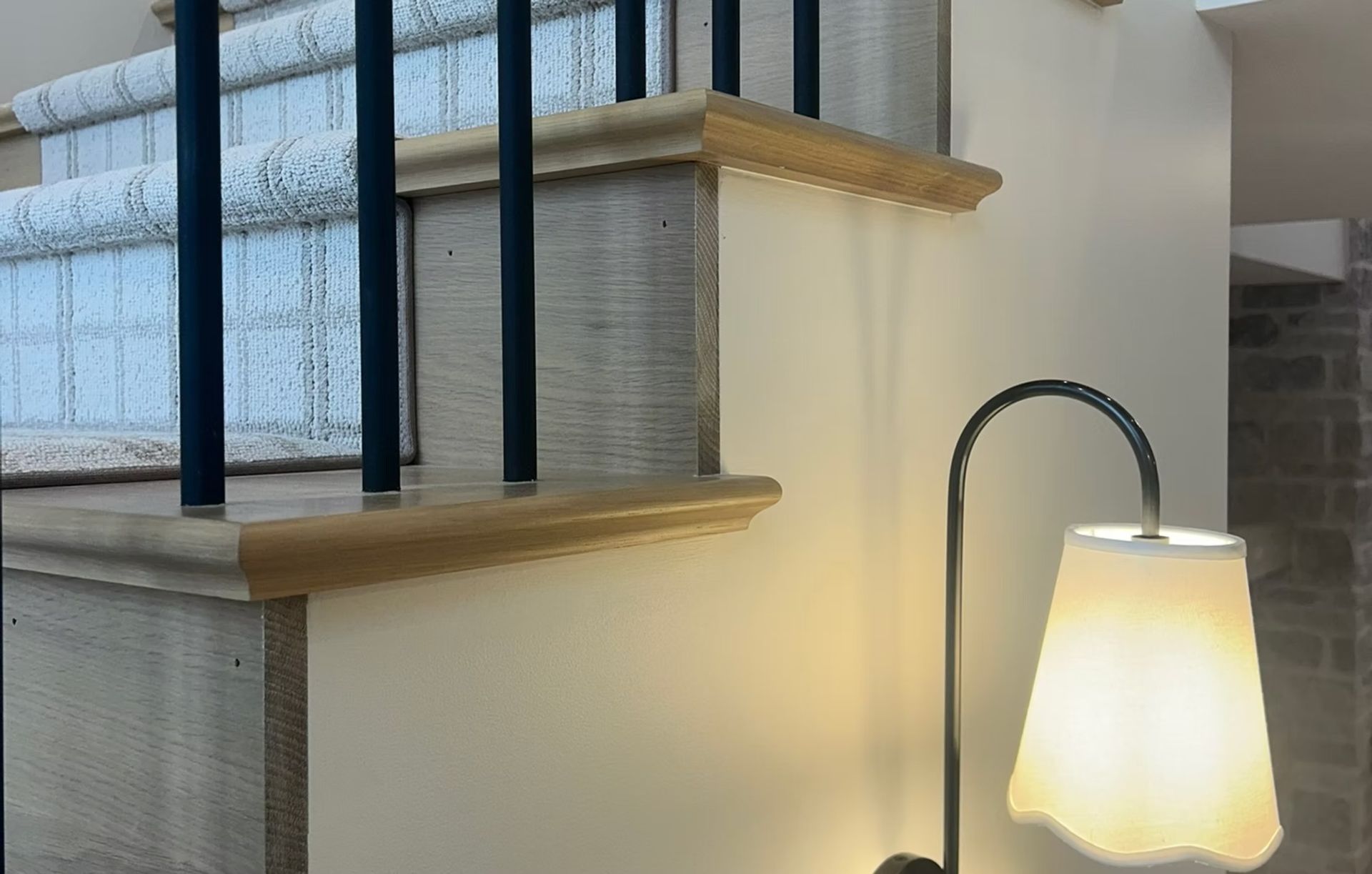 Stair landing with black railing, beige walls, and a glowing floor lamp beside a window with patterned blinds