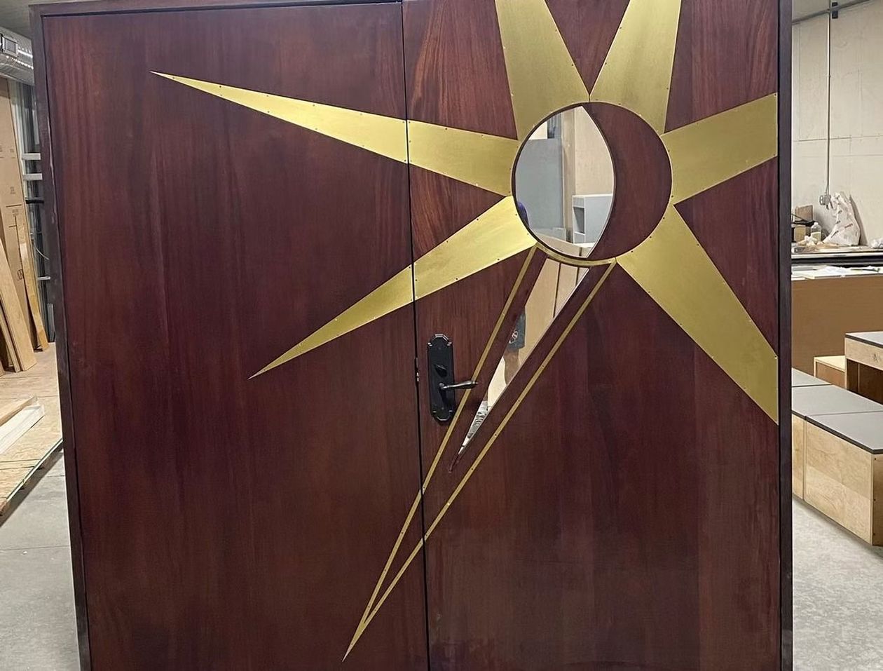 Wooden cabinet with a gold starburst design and circular mirror, standing in a workshop.