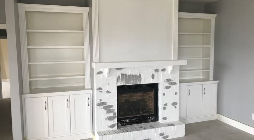 Built-in white bookshelves and cabinets flanking a white fireplace in a bright room