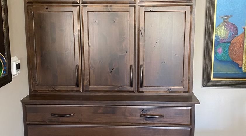 Wooden cabinet with three paneled doors and two drawers, against a wall beside a colorful framed painting.