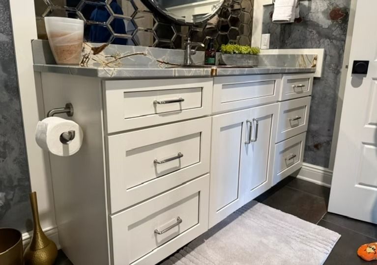 White bathroom vanity with cabinets, drawers, mirror, and countertop decor beside a toilet paper holder